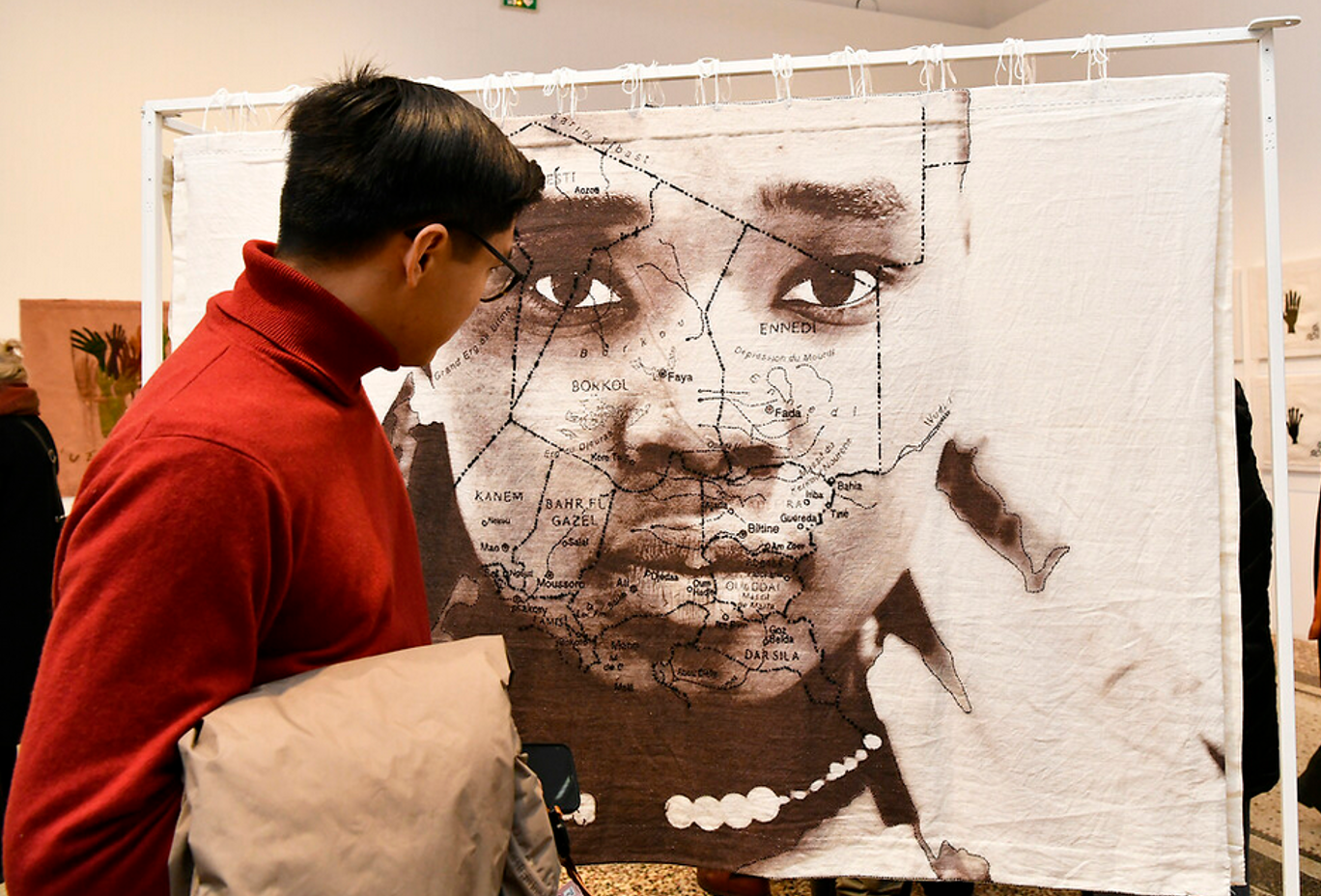 Un visiteur devant l'un des grands paravents mêlant photo et broderie et représentant un visage de femme