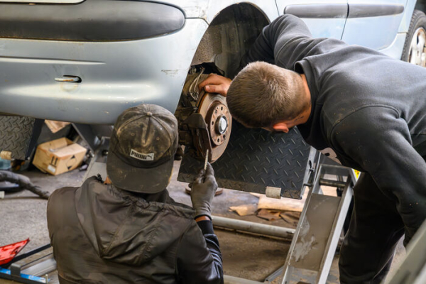deux "apprentis" mécaniciens travaillent sur une voiture au niveau des roues arrières